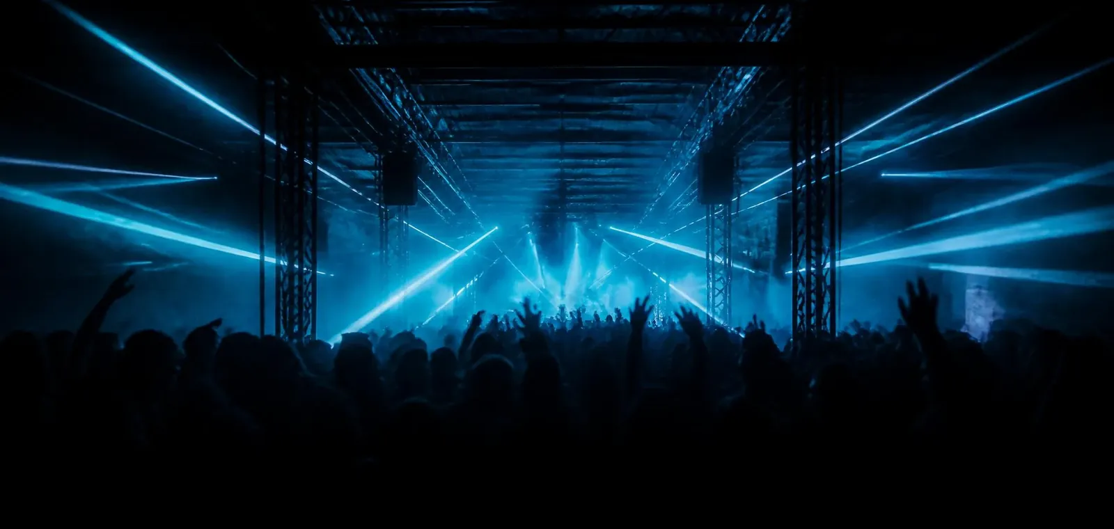 Crowd silhouetted against blue lasers at a TUMN1S warehouse set